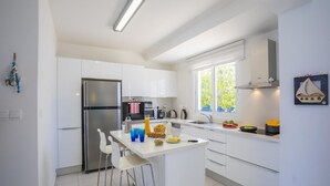 A modern kitchen with white cabinets, stainless steel appliances, and a central island with bar stools. - Protaras Seafront Villa Sirina Pearl (Paralimni)