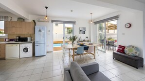 A modern kitchen with a washing machine, a refrigerator, and a dining area with a table and chairs. - Villa Kalimera in Protaras (Paralimni)