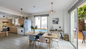 A modern kitchen with a dining area, large windows, and a view of a pool. - Villa Kalimera in Protaras (Paralimni)