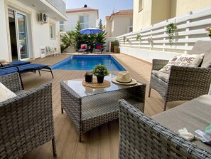 Área na piscina com móveis de vime, uma mesa com chapéu e um guarda-sol azul.