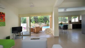 A spacious living room with a flat-screen TV, a dining area with a pool view, and a kitchen area. - Villa Michelle 8 in Protaras (Paralimni)