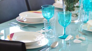 A dining table set with plates, cutlery, and blue glassware, accompanied by a vase of yellow flowers. - Villa Michelle 8 in Protaras (Paralimni)