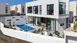 Una casa moderna de dos pisos con piscina, mobiliario exterior y un patio cubierto.