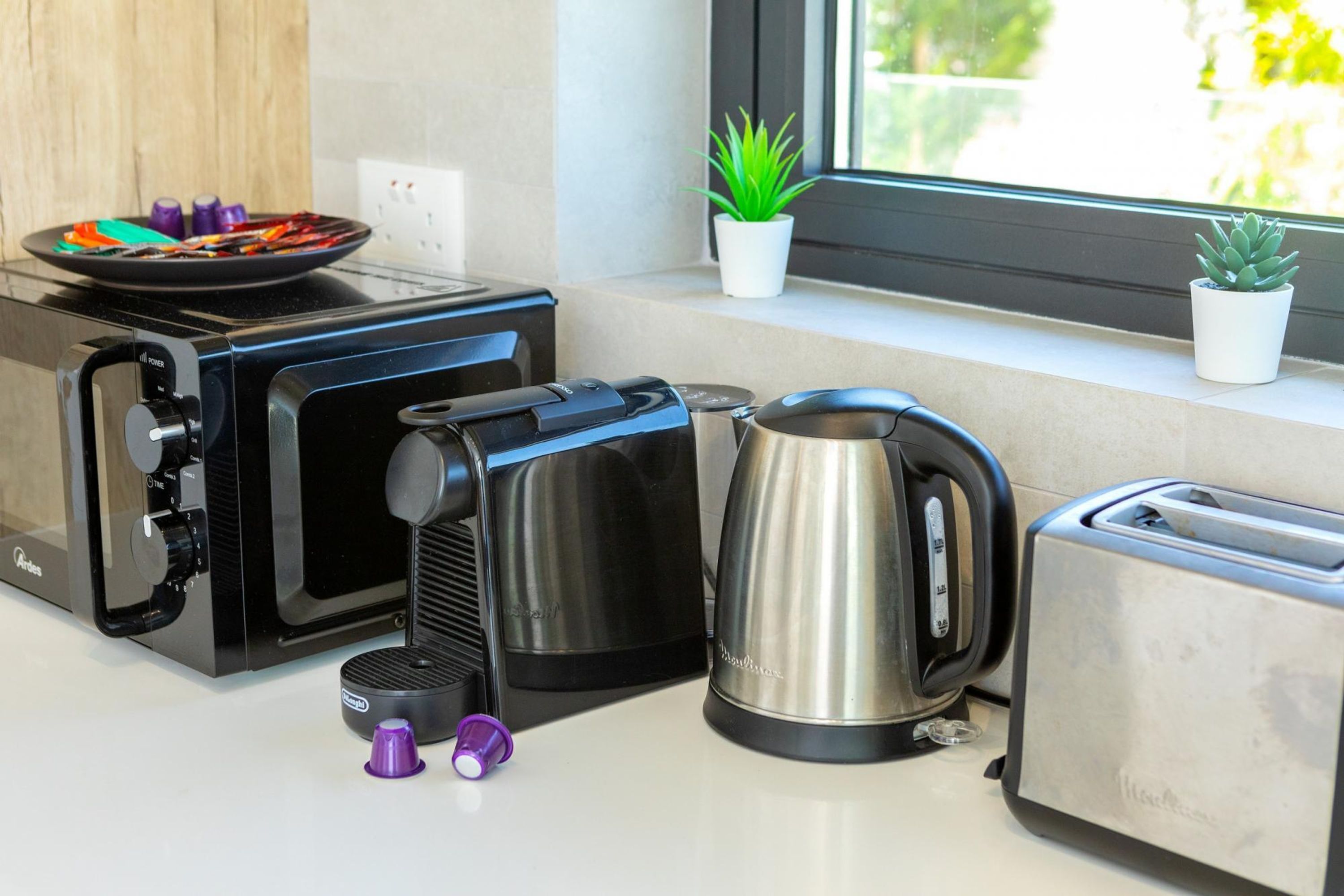 A kitchen with a coffee maker, kettle, toaster, and a window with plants.