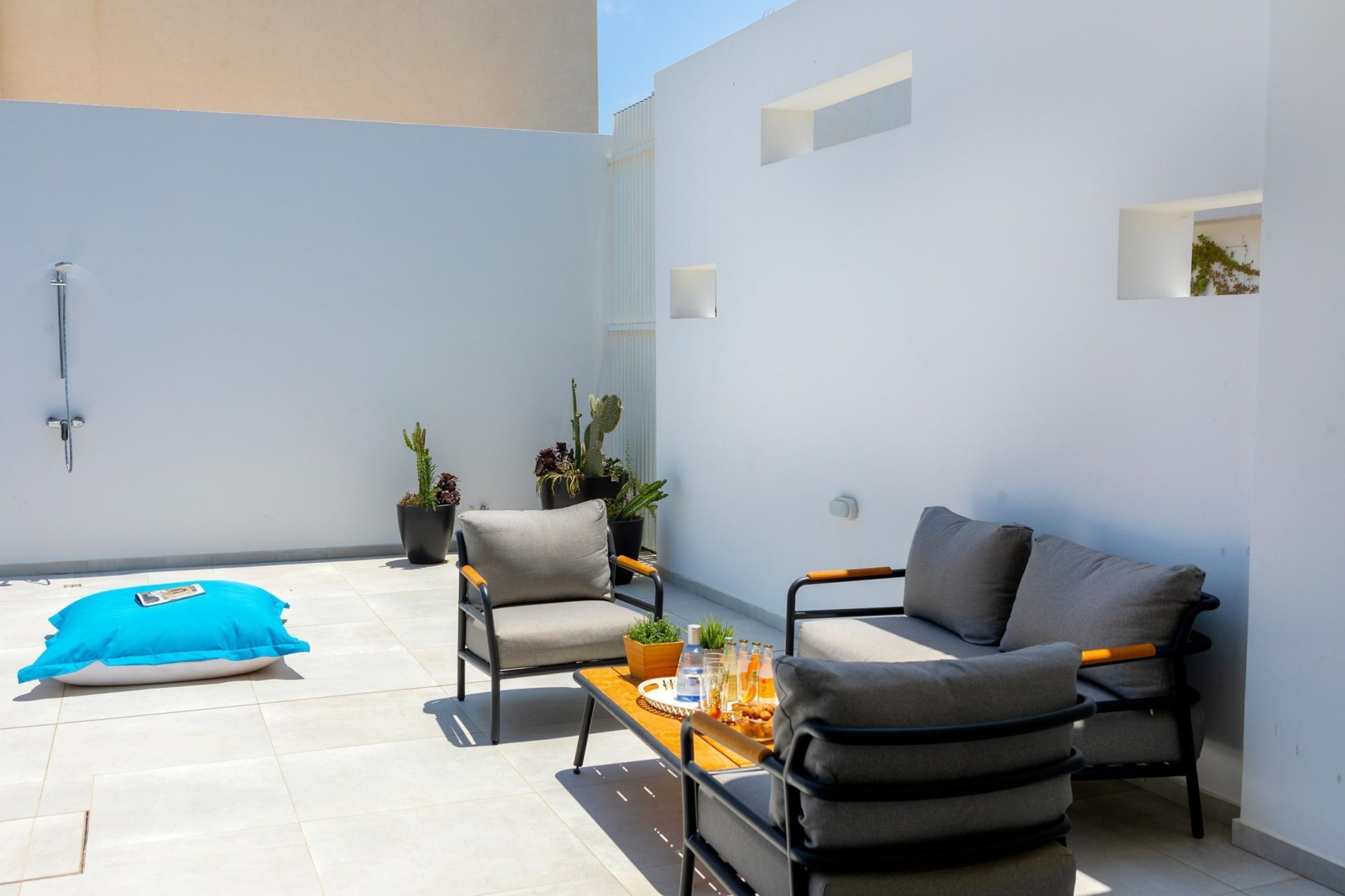 A modern outdoor seating area with a sofa, chairs, and a table. There are potted plants and a blue cushion on the floor.