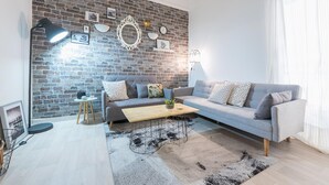 A modern living room with a brick wall, a grey sofa, a wooden coffee table, and a patterned rug. - Stylish 1BR Retreat in Central Athens (Athens)