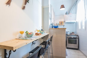 A compact kitchen with a wooden countertop, a stove, and a dining area with chairs.