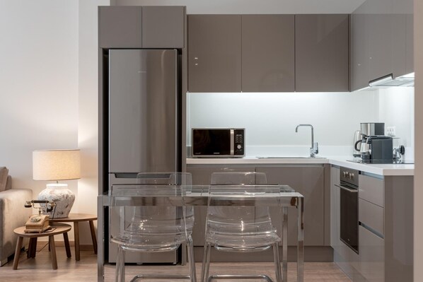 A modern kitchen with a built-in refrigerator, microwave, and coffee maker. There is a small dining area with a table and chairs.