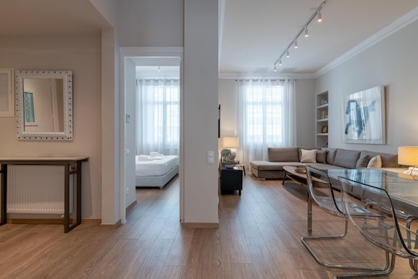 Een moderne woonkamer met een glazen eettafel, een bank, een bed en een spiegel.