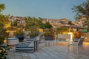 Terraço no telhado com área de estar, vasos de plantas e vista para a paisagem urbana.