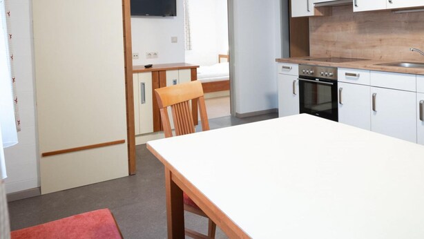A compact kitchen with a white countertop, wooden chairs, and a built-in oven. - Seilergasse Apartments - TOP 2 (Zell am See)