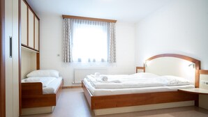 A bedroom with a wooden bed, a wooden nightstand, a built-in wardrobe, and a window with curtains. - Seilergasse Apartments - TOP 2 (Zell am See)