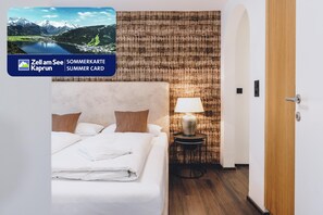 A hotel room with a bed, a lamp, a wooden door, and a view of a mountainous landscape. - Alpine City Living - TOP 11 (Zell am See)