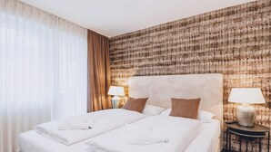 A hotel room with a large bed, two bedside lamps, a headboard, and a patterned wall. - Alpine City Living - TOP 11 (Zell am See)