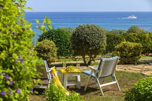 A garden with a table and chairs, a view of the sea, and a boat in the distance. - Sirina Lina Beachfront Suite (Paralimni)
