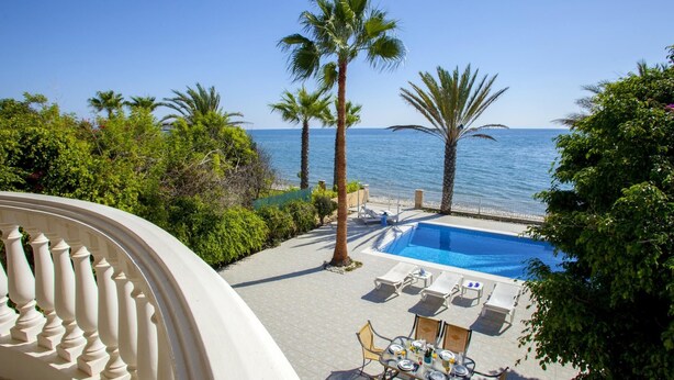 A pool area with lounge chairs and a table, overlooking the sea. - Sunset Beachfront Villa Meneou (Larnaca)