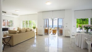 A spacious living area with a sofa, a dining table set for two, and a view of the sea through large sliding doors. - Sunset Beachfront Villa Meneou (Larnaca)