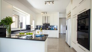 A modern kitchen with white cabinets, a black countertop, and stainless steel appliances. - Sunset Beachfront Villa Meneou (Larnaca)