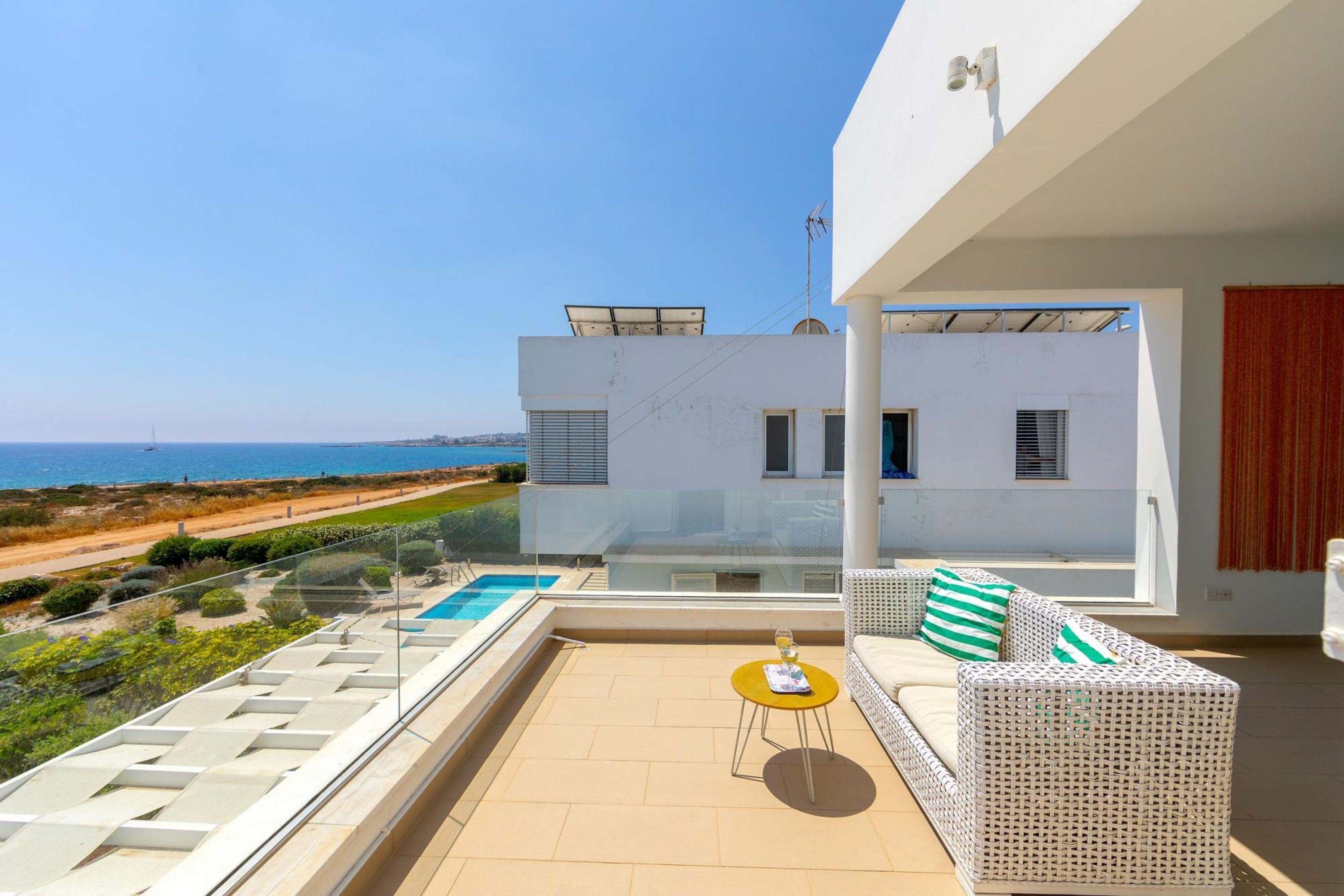 Varanda moderna com piscina, mobiliário de vime branco e vista clara para o mar.