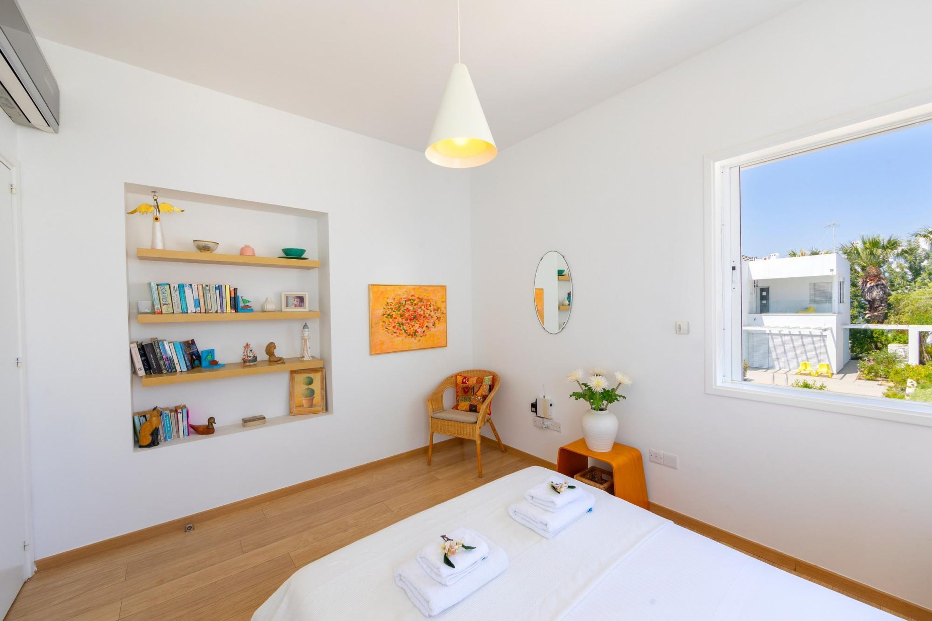 A modern bedroom with a large bed, a bookshelf, a chair, and a window with a view of the outside.