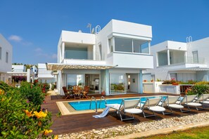 Une maison moderne à deux étages, dotée d’une piscine, d’un espace salon extérieur et d’un jardin.
