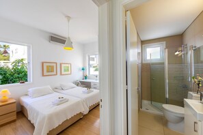 Une chambre moderne avec deux lits, une table de chevet, une fenêtre donnant sur un espace verdoyant et une salle de bain avec douche et toilettes.