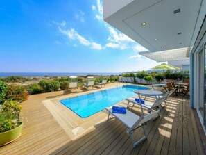 Un espace piscine avec vue sur la mer, des chaises longues et une table avec des parasols.