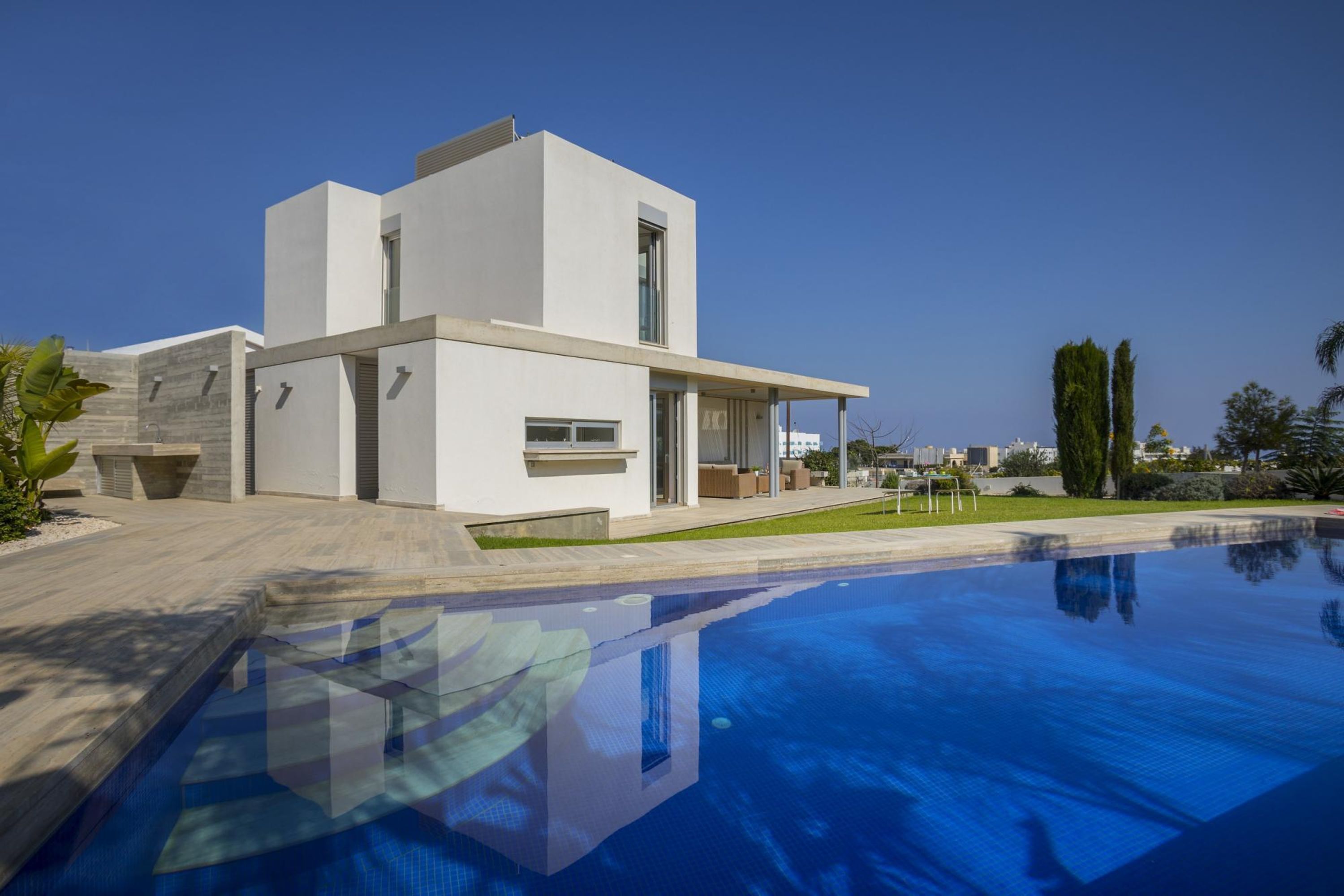 Ein modernes Haus mit Swimmingpool, großen Fenstern und einem gepflegten Rasen.