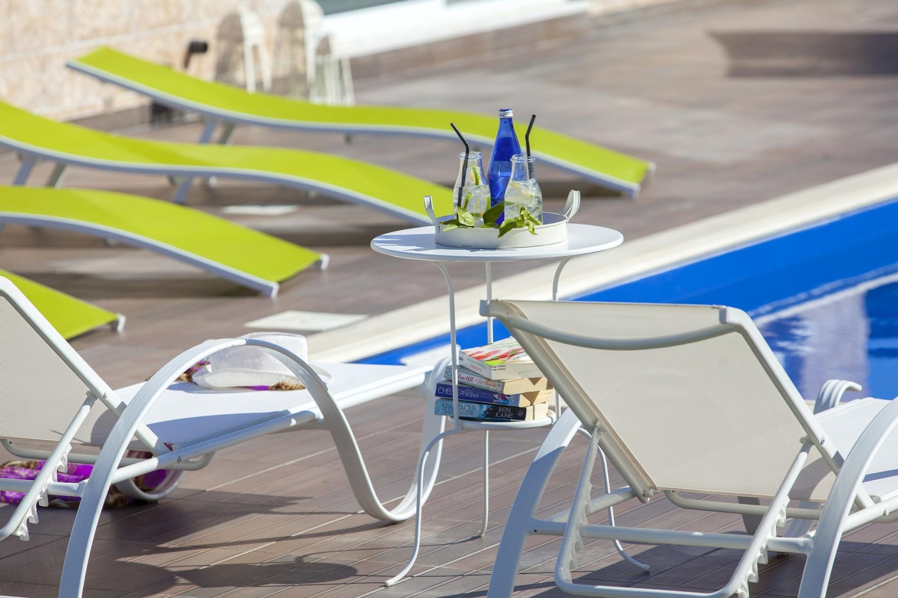 A poolside area with lounge chairs and a table with books and bottles.