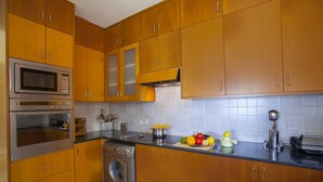 A kitchen with wooden cabinets, stainless steel appliances, and a fruit bowl on the counter. - Protaras Coast Panorama (Paralimni)