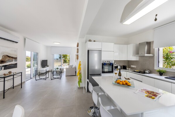 Een moderne keuken met witte kasten, een groot eiland en een eethoek met barstoelen.