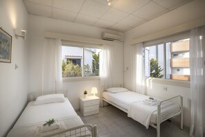 Two single beds with white mattresses and matching pillows, a bedside table, and a potted plant.