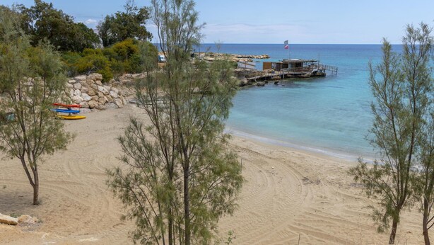 Una playa con un promontorio rocoso, un muelle y kayaks.