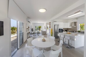 Een moderne keuken met een centraal eiland, witte kastjes en een eethoek met witte stoelen.