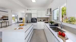 Una cocina moderna con armarios blancos, una isla central y un amplio ventanal con vistas a zonas verdes.