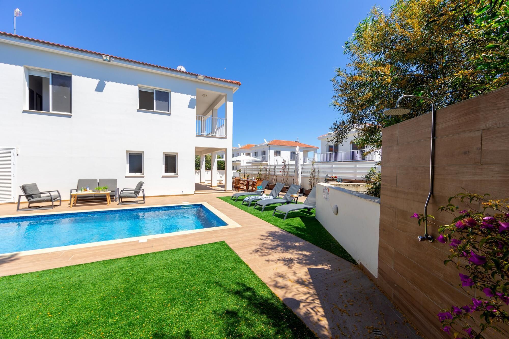 Une maison à deux étages avec une piscine, un espace salon extérieur et une clôture en bois.