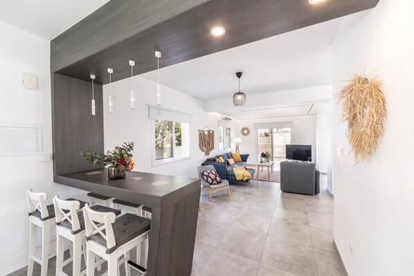 A modern kitchen with a central island, bar stools, and a dining area with a table and chairs.