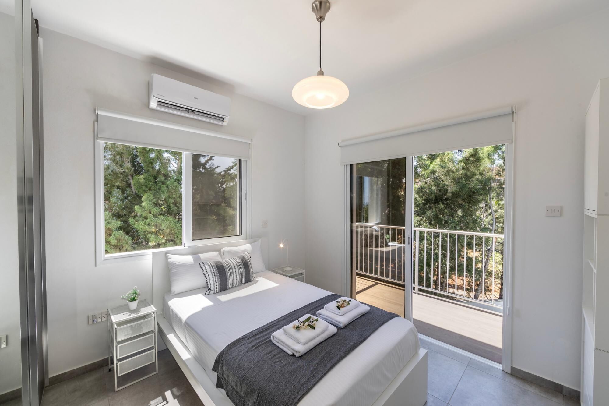 Ein modernes Schlafzimmer mit einem großen Bett, einem Nachttisch, einer Klimaanlage, einer Deckenleuchte und einem Balkon mit Geländer.