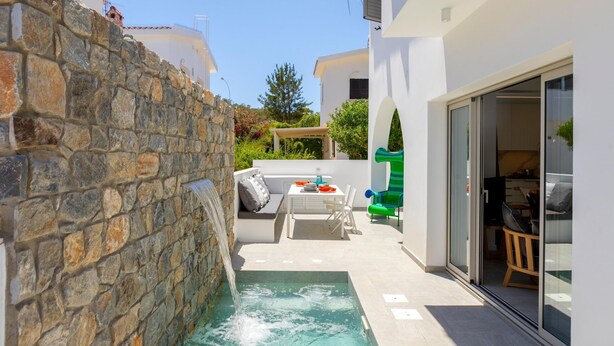A modern outdoor area with a stone wall, a small pool, and a seating area with a table and chairs. - Protaras Rose By The Sea Villa (Paralimni)