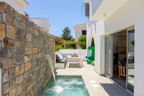 Un espace extérieur moderne agrémenté d’un mur en pierre, d’une petite piscine et d’un coin salon avec une table et des chaises.