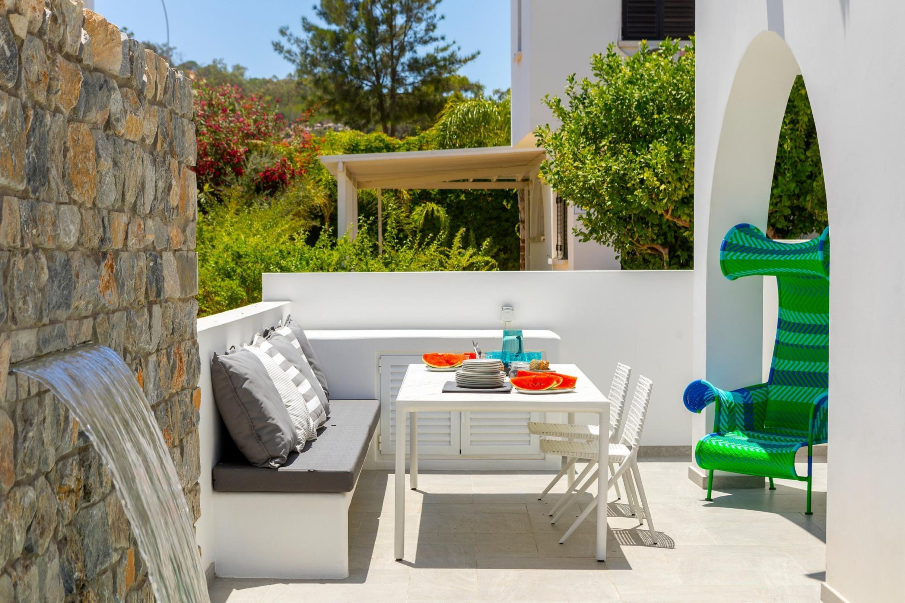 A patio with a stone wall, white furniture, a table with plates and a bowl, and a green chair.