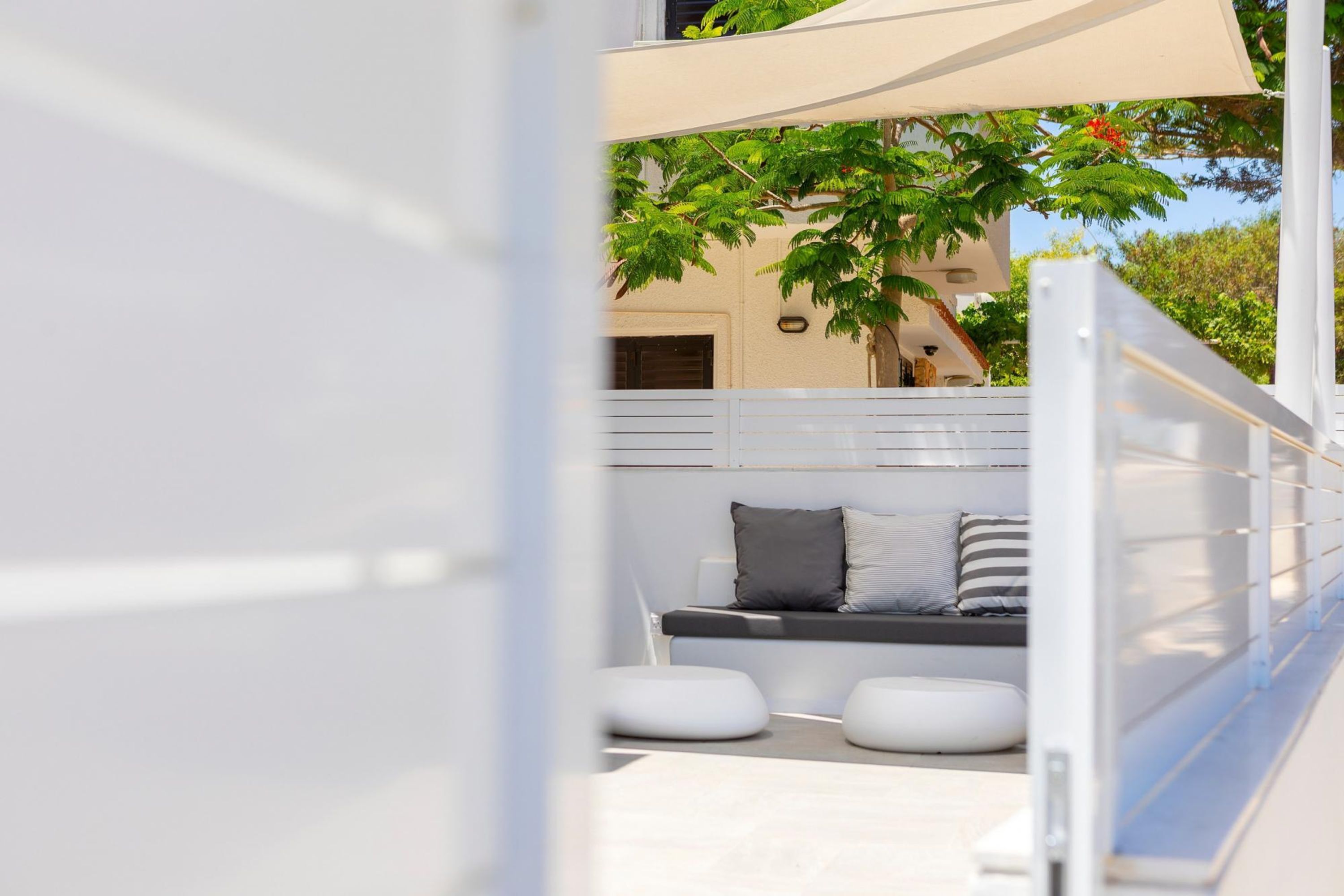 Un espacio moderno para sentarse al aire libre con un banco blanco, cojines y un toldo.