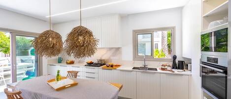 A modern kitchen with white cabinetry, a dining area with a table and chairs, and a large window providing natural light.