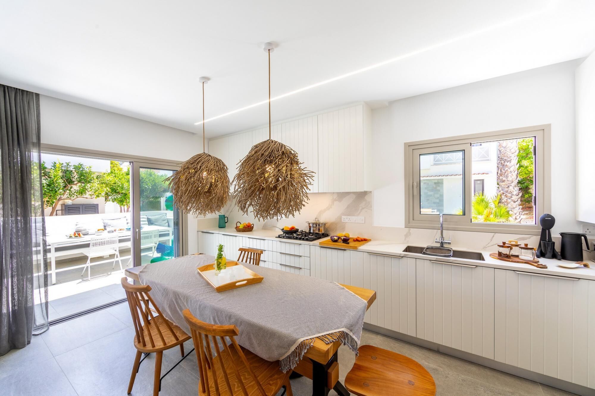 Une cuisine moderne avec des meubles blancs, un coin repas comprenant une table et des chaises, et une grande fenêtre donnant sur un paysage verdoyant.