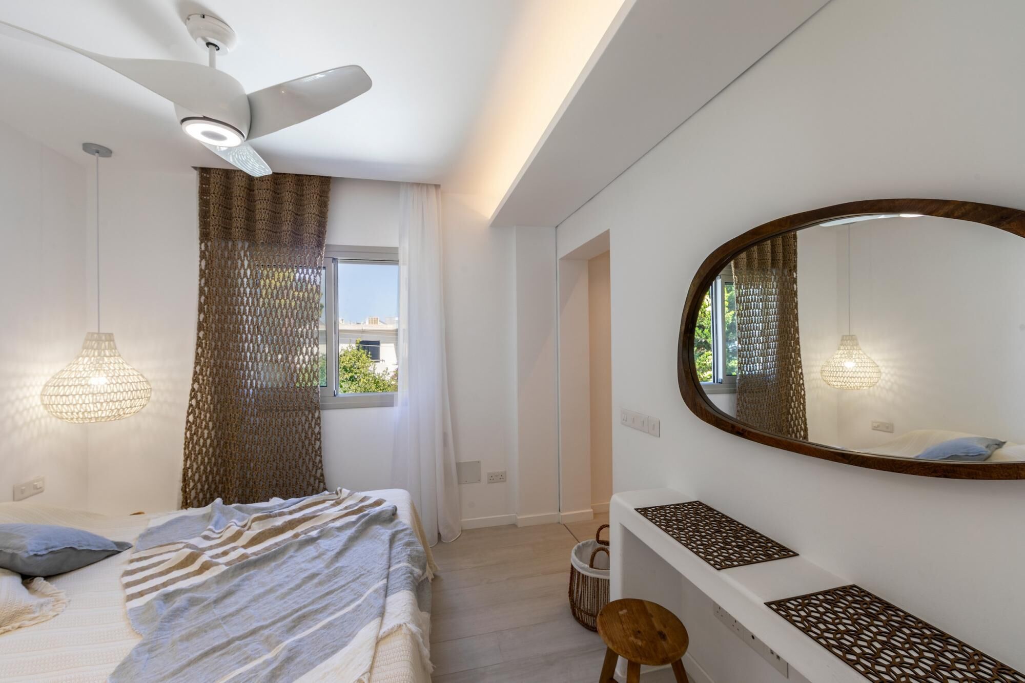 A modern bedroom with a bed, a ceiling fan, a large mirror, and a window with curtains.
