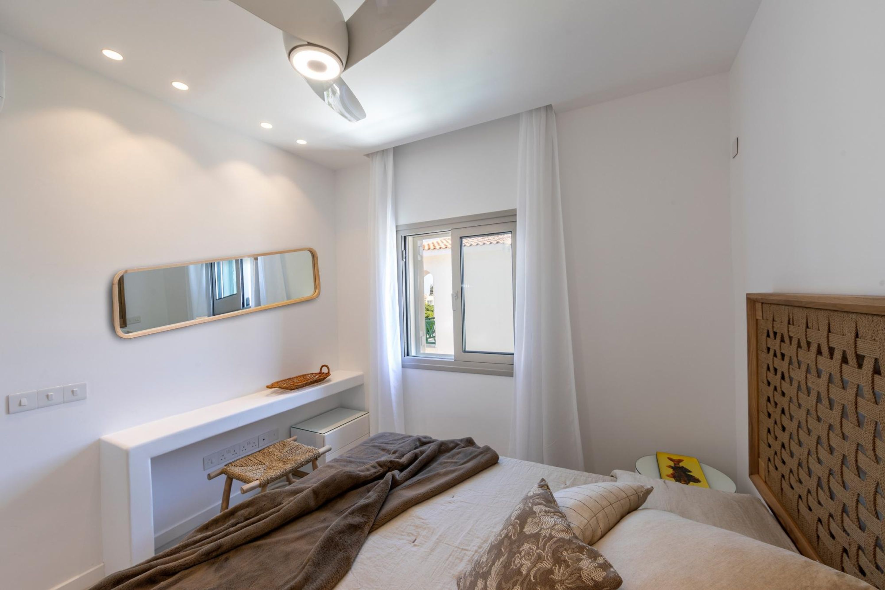 Una camera da letto con un letto, un comodino, uno specchio, una finestra con tende e una testiera con motivo intrecciato.