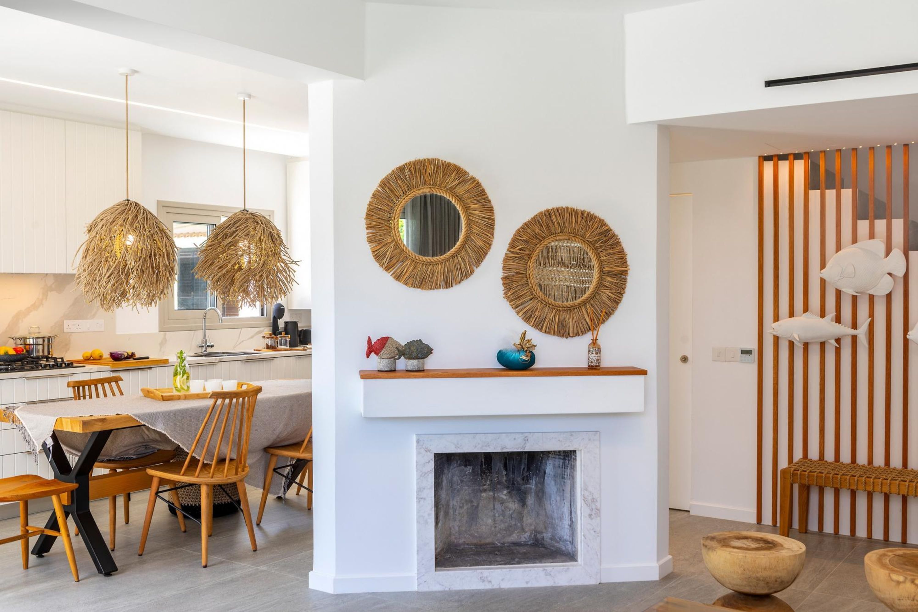 A modern kitchen with white cabinetry, a dining area with wooden chairs and a table, and a fireplace with decorative mirrors.