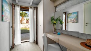 Ein modernes Zimmer mit einer Schiebetür zu einem Außenbereich, ein kleiner Tisch mit einer Vase und einem Hut, und ein Spiegel an der Wand.