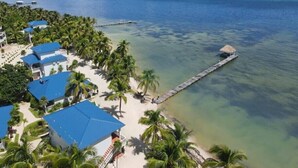 A coastal resort with multiple blue-roofed buildings, a pier extending into the ocean, and a sandy beach lined with palm trees. - 1BR Seaside Casita @ Sapphire Beach Resort (San Pedro Town)