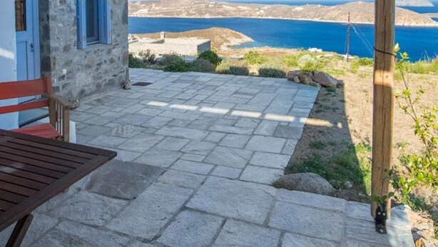 Un edificio de piedra con una pérgola de madera, un patio de piedra y vistas al mar.